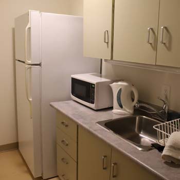 A private kitchenette featuring a large fridge, sink and large white cabinetry