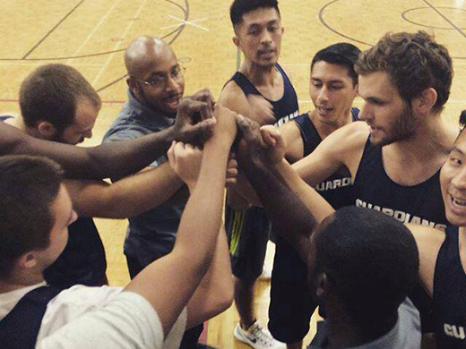 A huddle of Tyndale basketball players on the court with their hands together in the centre