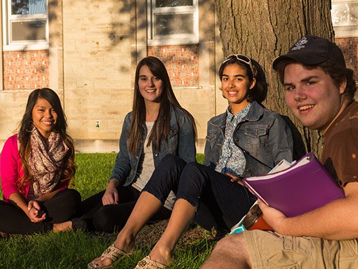 Four young students sitting on the grass under a tree