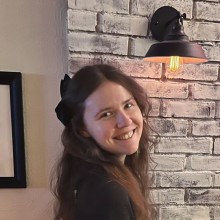 Molly standing in front of a break fireplace with a lamp on the wall.