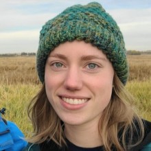 Nicole with a knit hat on standing in front of a field.